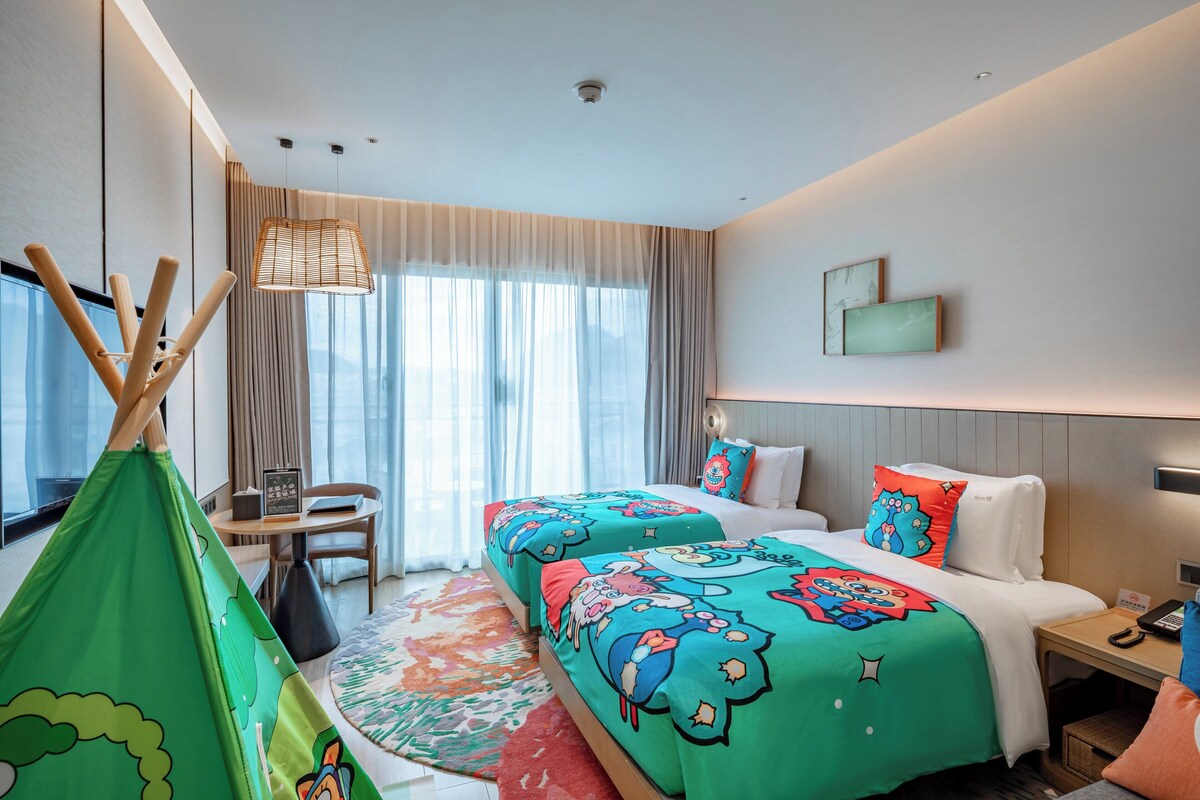 A hotel room with a bed, a desk, a chair, a window with curtains, and a view of the outdoors.