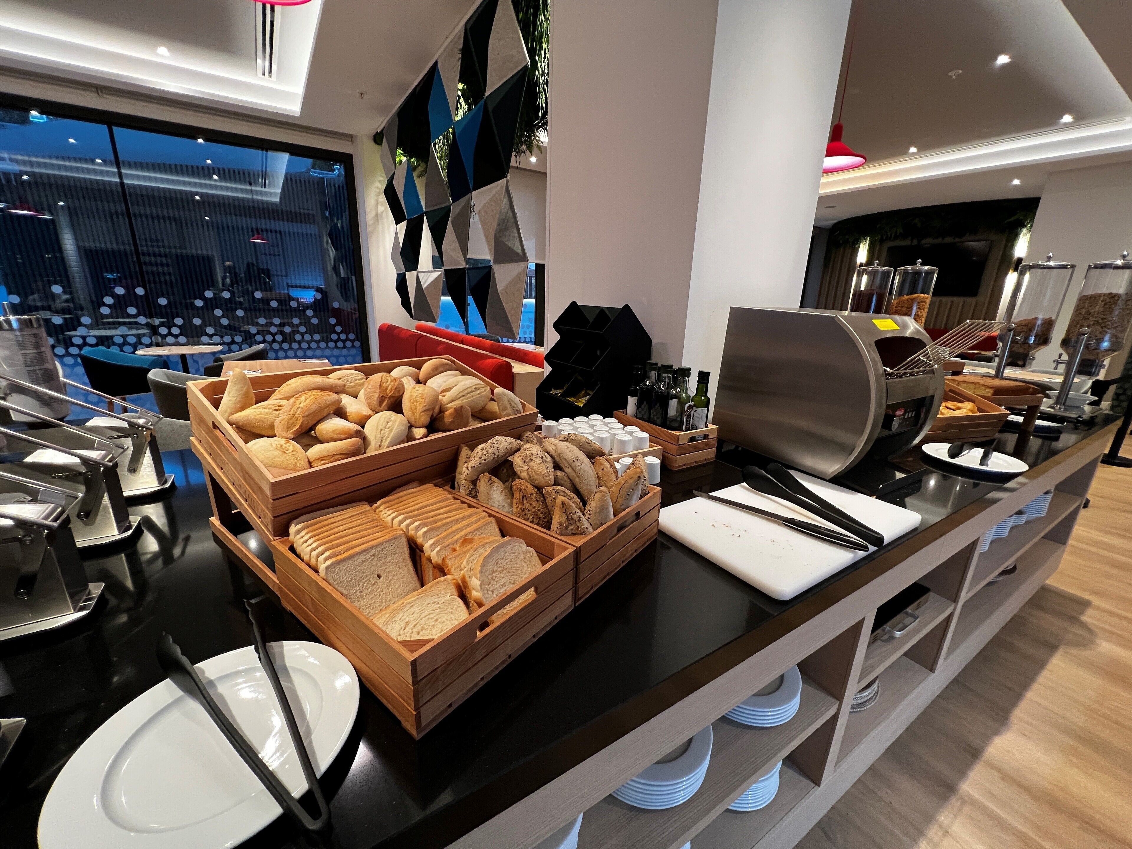 A buffet area with various bread and pastries, a coffee machine, and condiments.