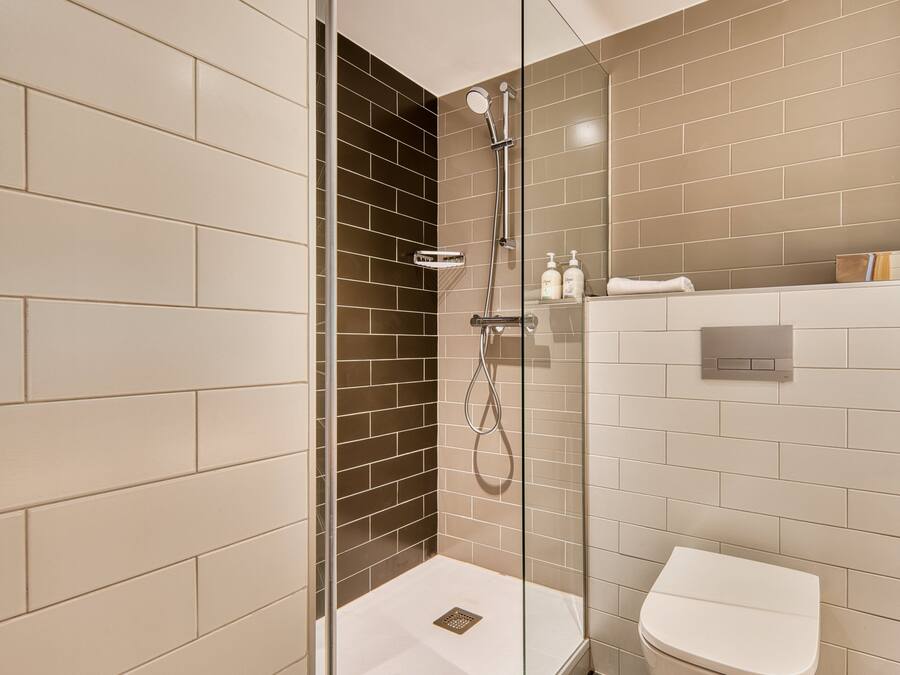 A modern bathroom with a glass-enclosed shower, a white toilet, and a tiled wall with a mix of beige and dark brown tiles.