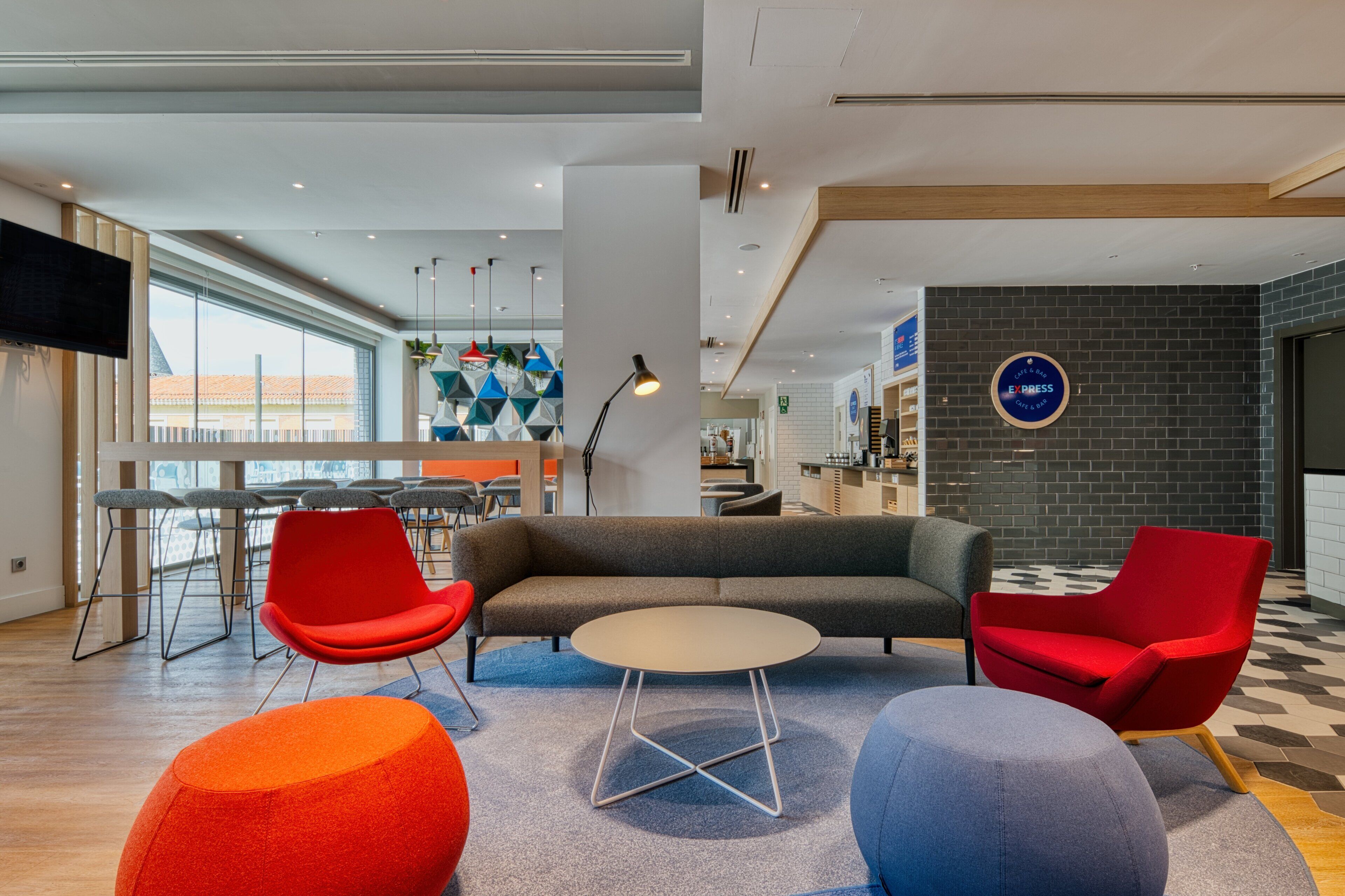 A modern lounge area with a sofa, red chairs, a round table, and a checkered floor.