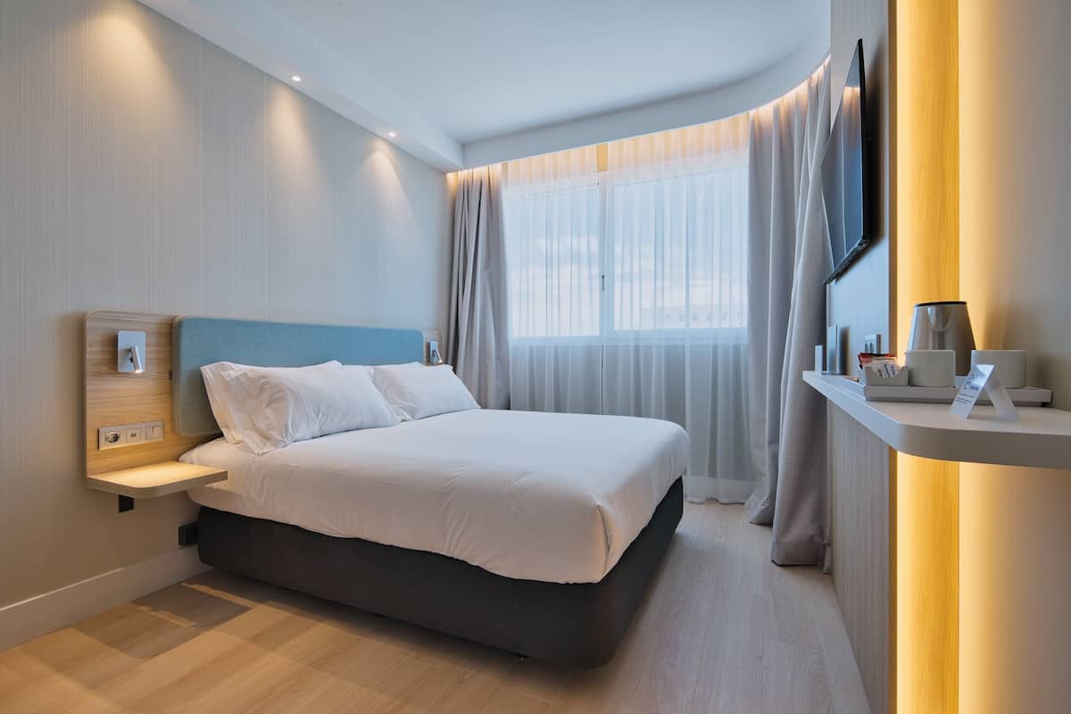 A modern hotel room with a large bed, bedside table, and a TV mounted on the wall.