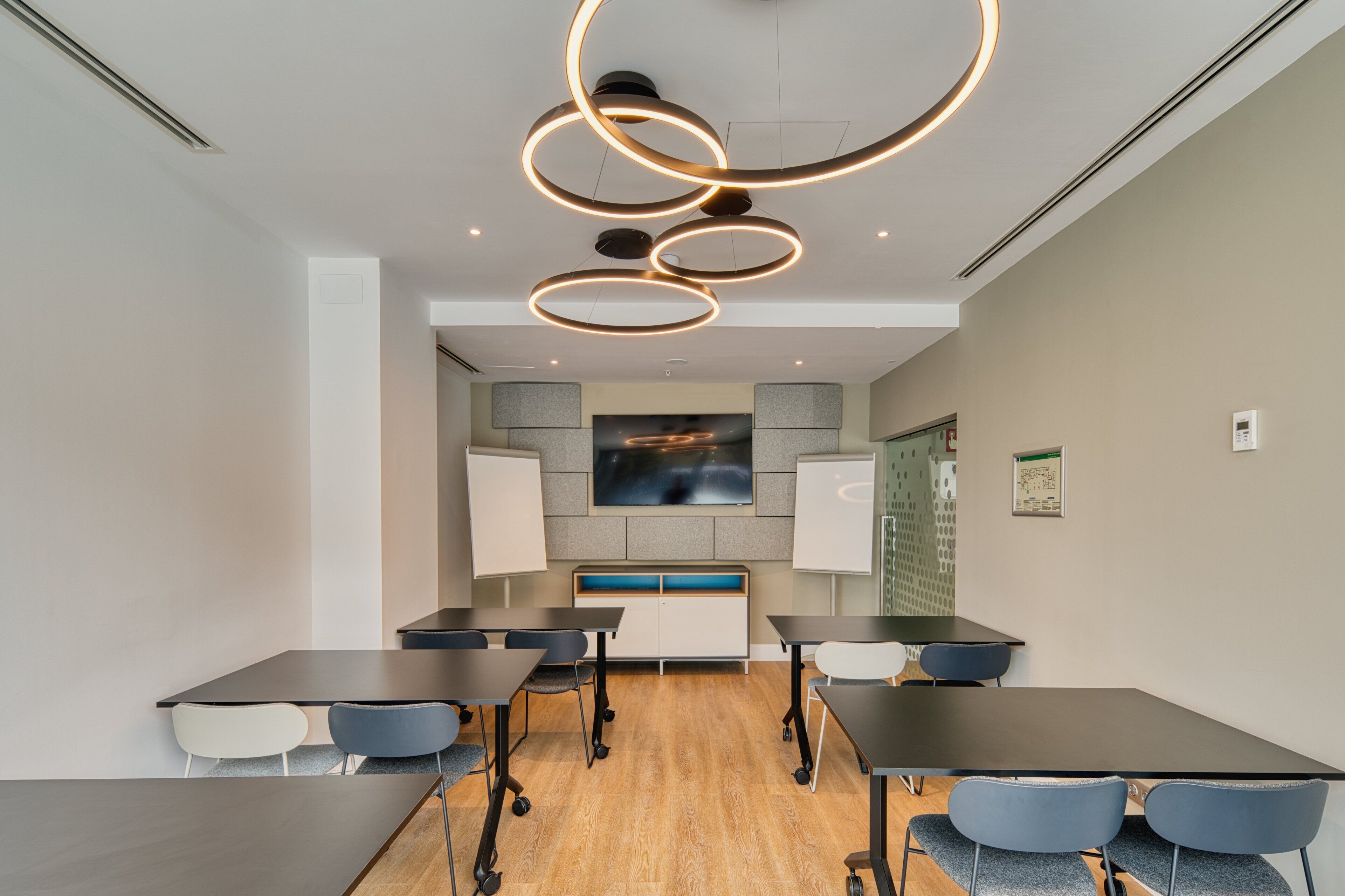 Una sala de conferencias con diseño moderno, que incluye una mesa central, sillas alrededor, un televisor de pantalla plana grande y una lámpara circular original.