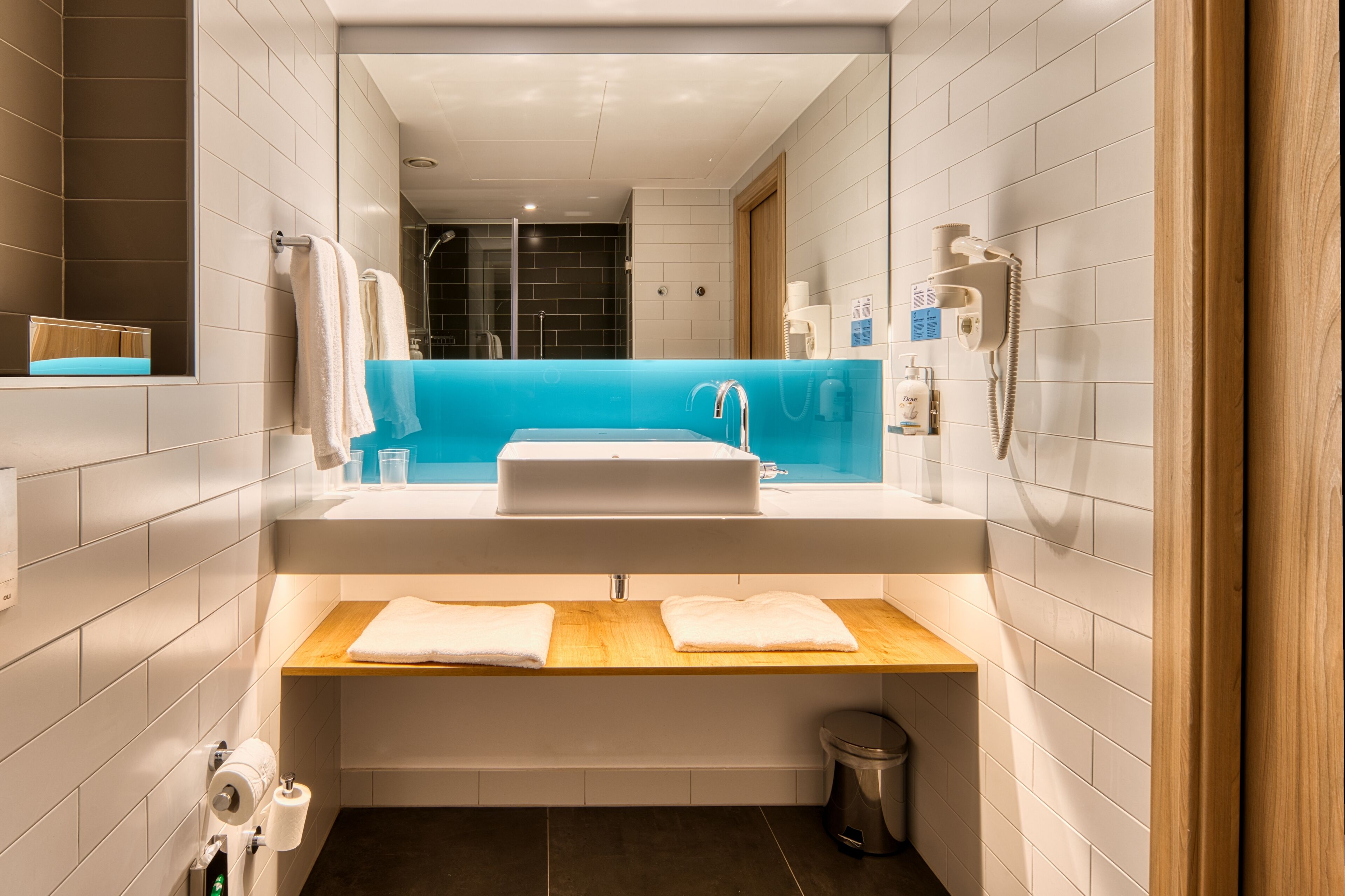 A modern bathroom with a large sink, a mirror, a blue accent wall, and a shower area visible through the glass door.