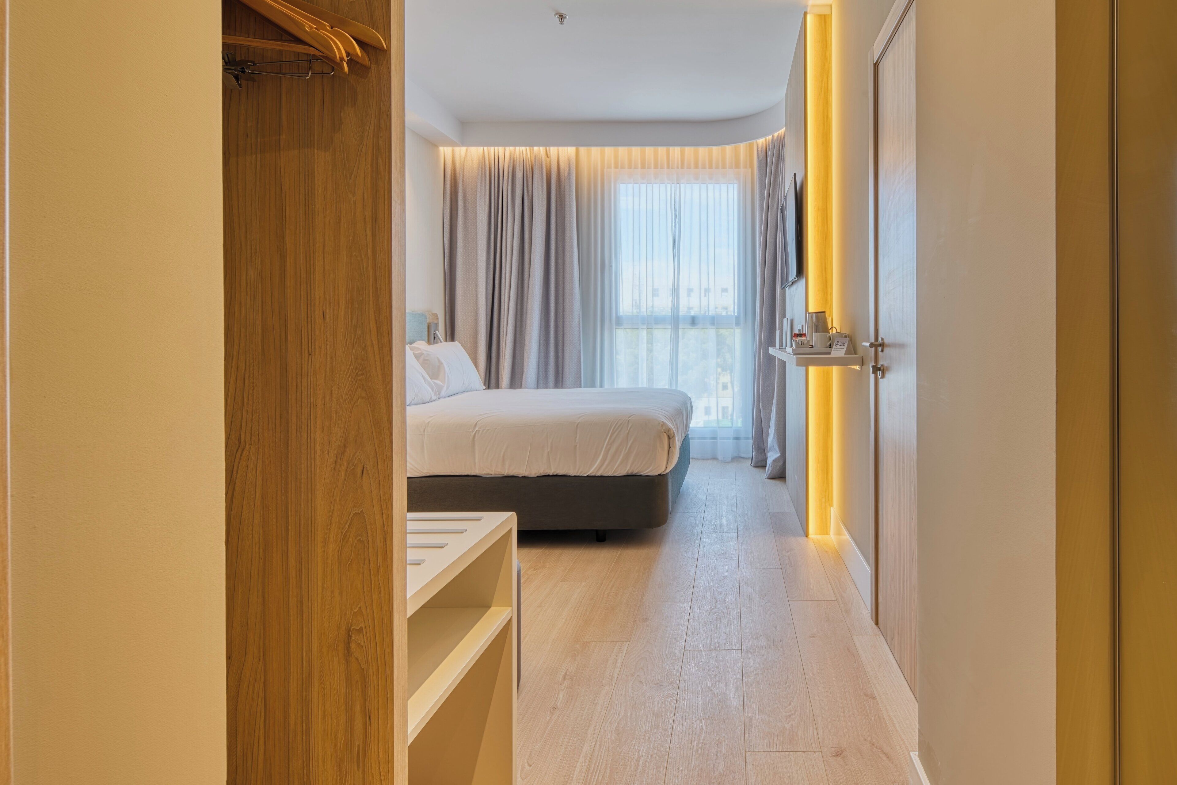 Ein Hotelzimmer mit einem Bett, einem Nachttisch, einem Kleiderschrank und einem fenster mit Vorhängen.