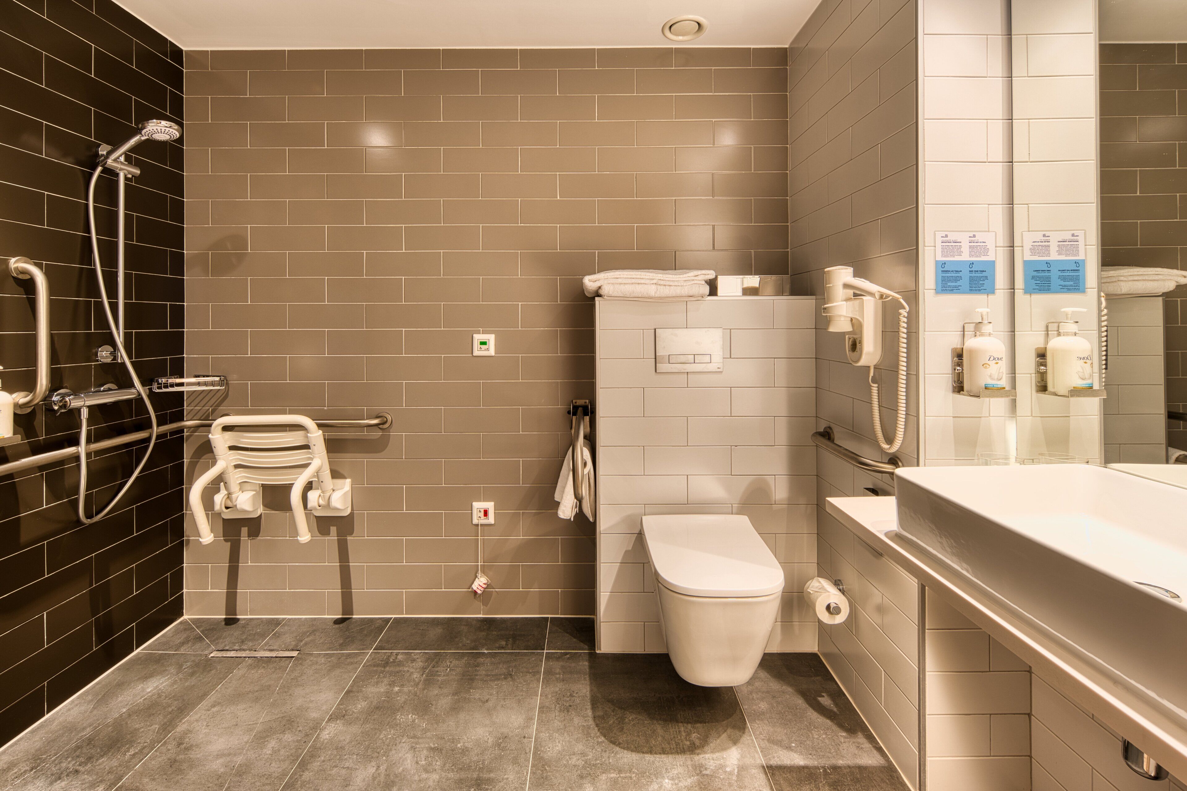 Een moderne badkamer met douche, toilet en wastafel, met een spiegel, handdoekhouder en handdroger.