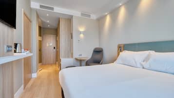 Habitación de hotel con una cama grande, un escritorio, una silla y un televisor montado en la pared.