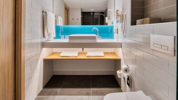 Un baño moderno con un lavabo blanco, tocador de madera y una pared de acento azul.