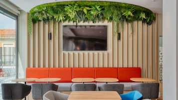 Un interior moderno con una zona de estar, un televisor de pantalla plana y una pared verde cubierta de plantas.