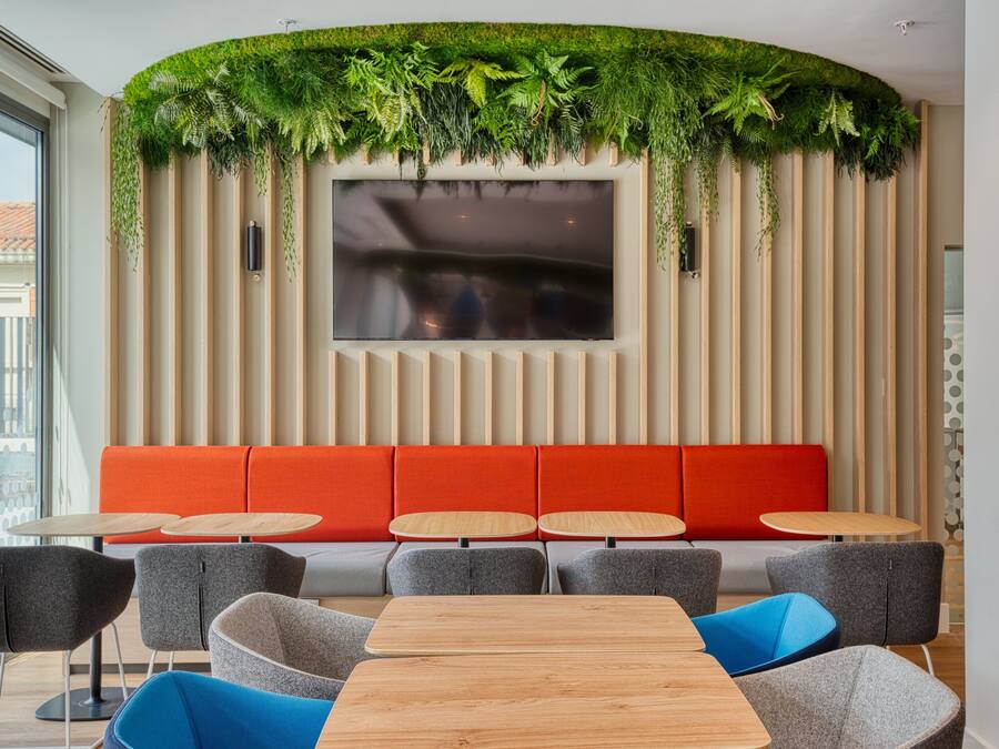 Un interior moderno con una zona de estar, un televisor de pantalla plana y una pared verde cubierta de plantas.