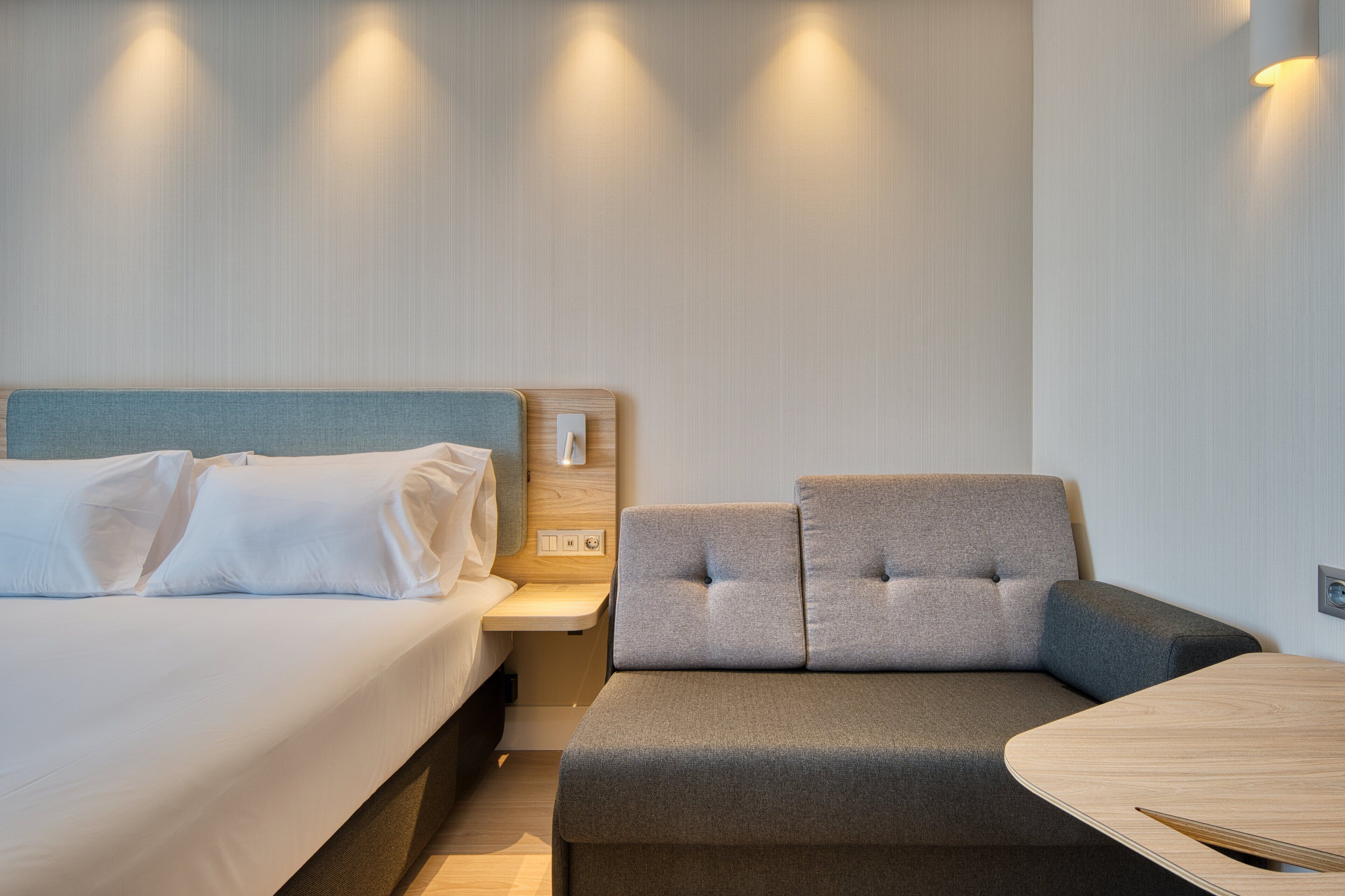 A modern hotel room with a bed, a sofa, and a small table.