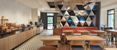 A modern cafe with wooden tables and chairs, a red sofa, and a geometric wall design.