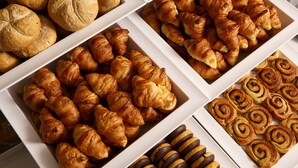 Une variété de viennoiseries, notamment des croissants, des petits pains et des pains à la cannelle, présentés dans des boîtes blanches.