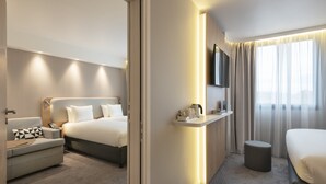 Une chambre d’hôtel moderne équipée d’un lit, d’un canapé, d’un bureau, d’une télévision et d’une fenêtre avec des rideaux.