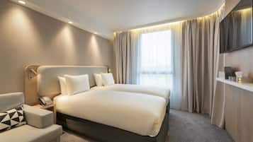 A modern hotel room with a large bed, a bedside table with a phone, a small sofa, and a TV mounted on the wall.