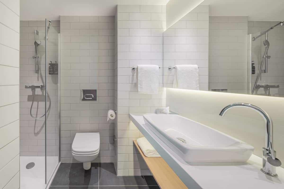 A modern bathroom with a glass-enclosed shower, a white toilet, a large sink with a mirror, and a towel rack.