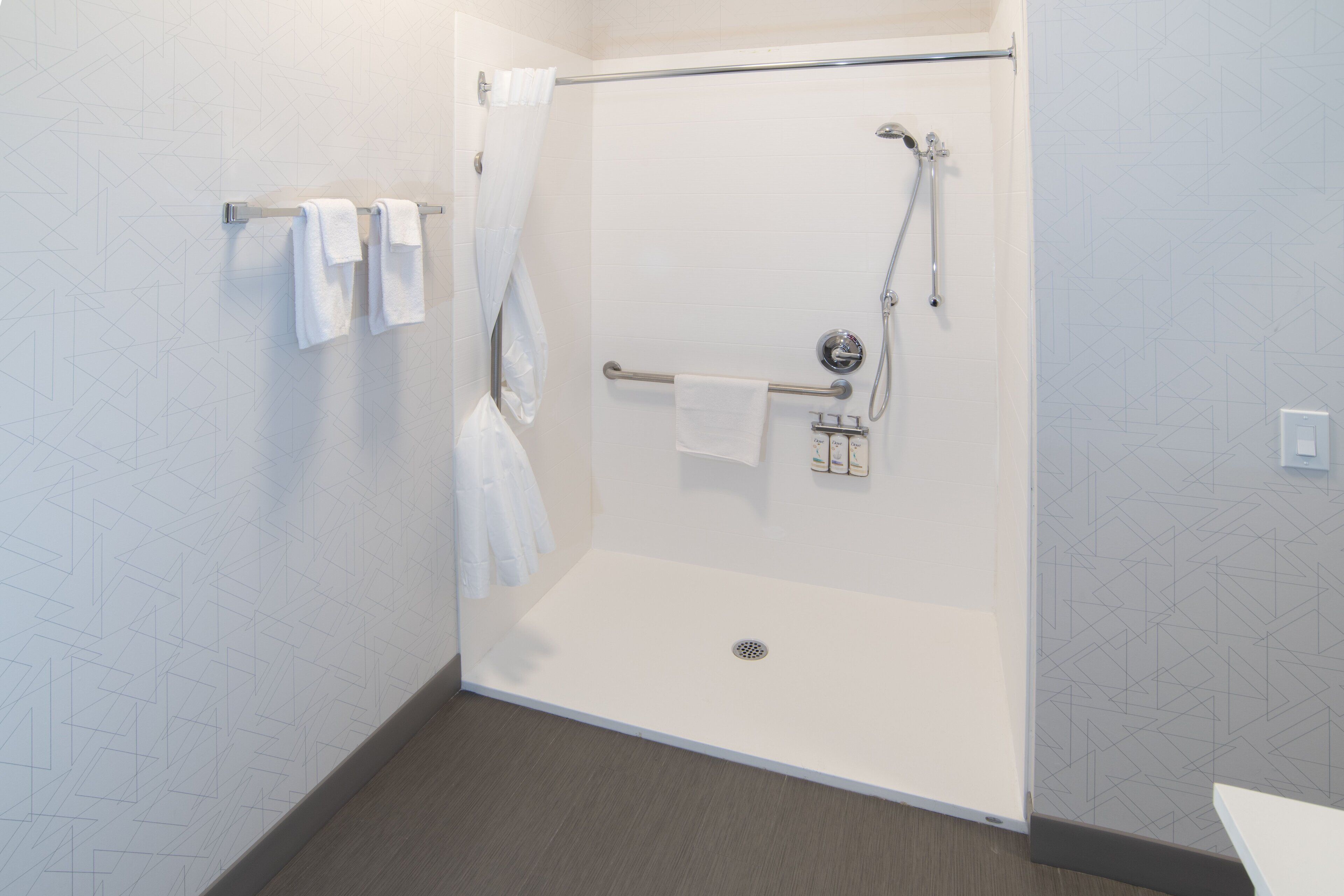 Une salle de bain moderne dotée d’une douche à l’italienne, d’un porte-serviettes avec plusieurs serviettes et d’une barre d’appui.