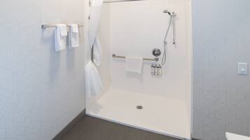 Une salle de bain moderne dotée d’une douche à l’italienne, d’un porte-serviettes avec plusieurs serviettes et d’une barre d’appui.