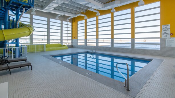 An indoor swimming pool with a yellow and blue color scheme, large windows, and a lifeguard station. - Holiday Inn Express and Suites Moose Jaw by IHG (Moose Jaw)