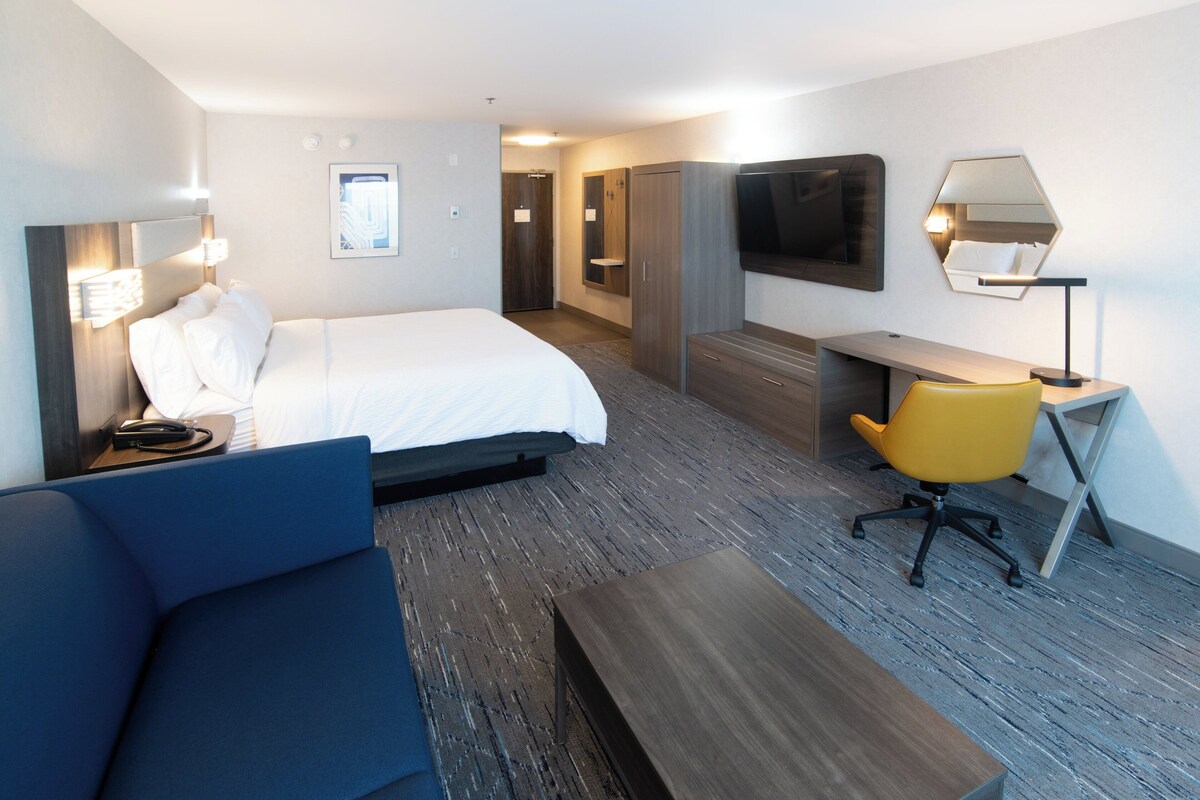 A hotel room with a bed, a desk, a chair, a TV, and a wardrobe.
