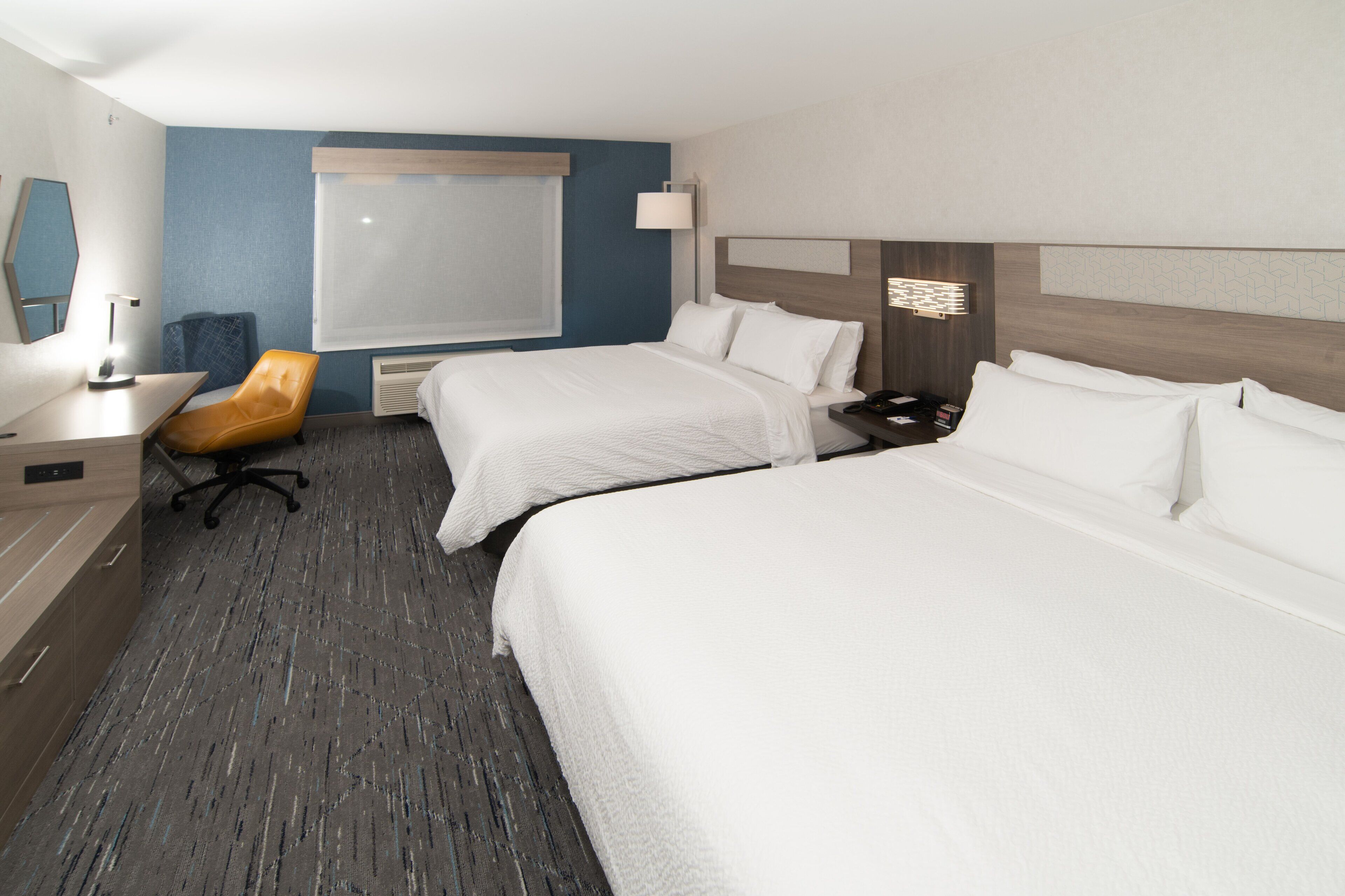 A hotel room with two beds, a desk, a chair, and a window.