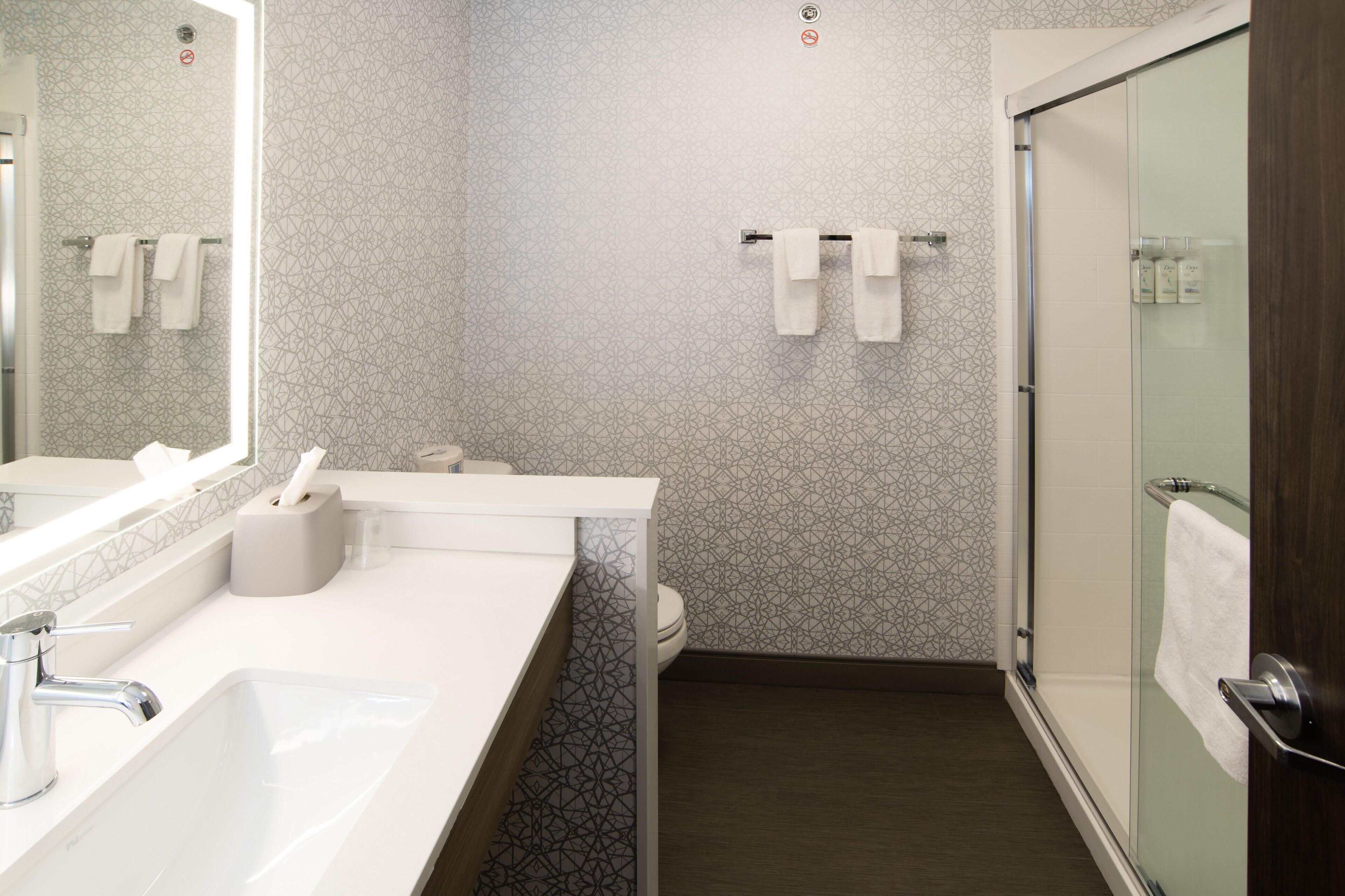 A modern bathroom with a white sink, a mirror, a toilet, and a glass shower enclosure.