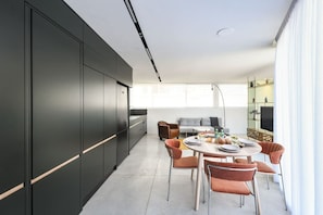 Une cuisine moderne avec des meubles de couleur sombre et un coin repas comprenant une table ronde et des chaises orange.