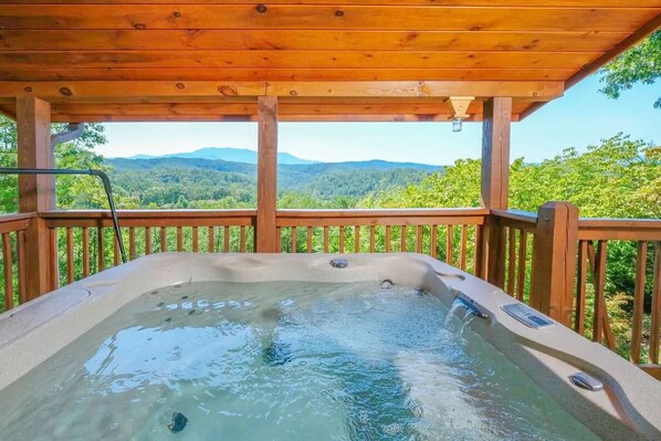 A hot tub with a wooden deck and a view of a forested mountain range.