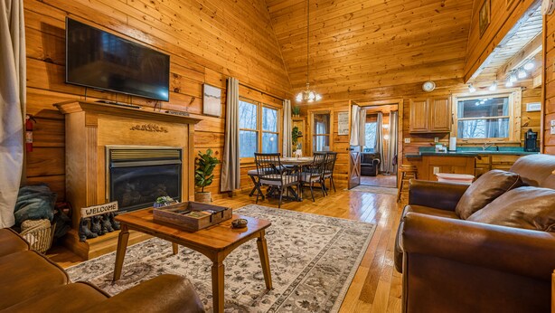 A log cabin interior with a fireplace, a television mounted above it, a dining area with a table and chairs, and a living room with a sofa and a coffee table. - NEW listing! INDOOR POOL, panoramic views, & game room - 15 min to Pigeon Forge (Sevierville)