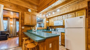 A wooden cabin interior with a kitchen featuring wooden cabinets, a large island with stools, a refrigerator, and a dining area with a table and chairs. - NEW listing! INDOOR POOL, panoramic views, & game room - 15 min to Pigeon Forge (Sevierville)