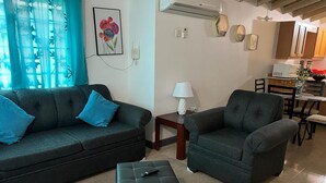 A living room with two dark sofas, a small table with a lamp, and a remote control on a ottoman. - Vacation Home Rental (Florence Hall Village)
