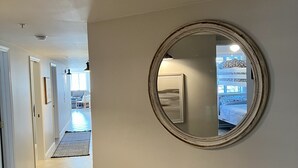 Ein Flur mit einer Bank, einem runden Spiegel an der Wand und Blick in einen Raum mit einem Bett und gemusterten Vorhängen.