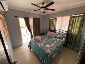 A bedroom with a bed, curtains, a ceiling fan, and a nightstand.