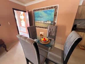 Un comedor con una mesa de vidrio, dos sillas tapizadas y un cuadro con una playa.
