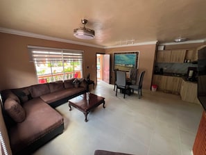 A living room with a brown sofa, a wooden coffee table, and a dining area with a chair and table.