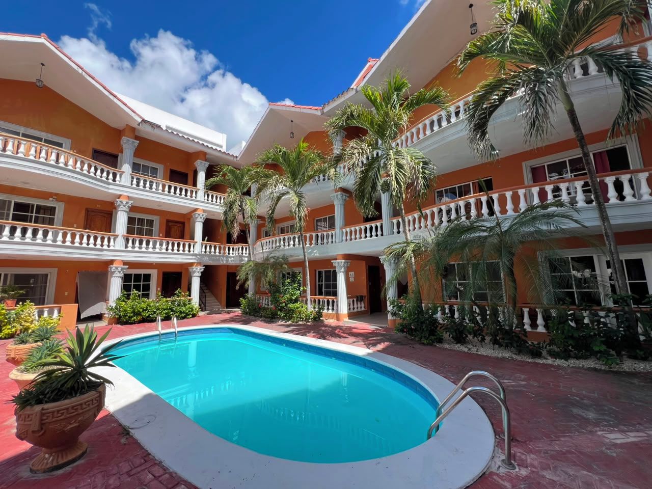 A hotel with a central swimming pool, multiple balconies, and palm trees.