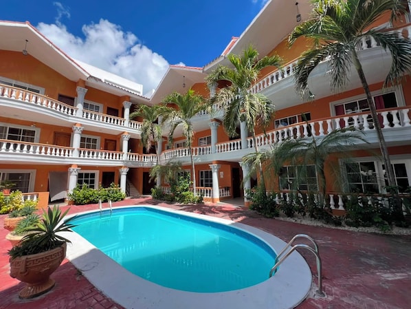 A hotel with a central swimming pool, multiple balconies, and palm trees.