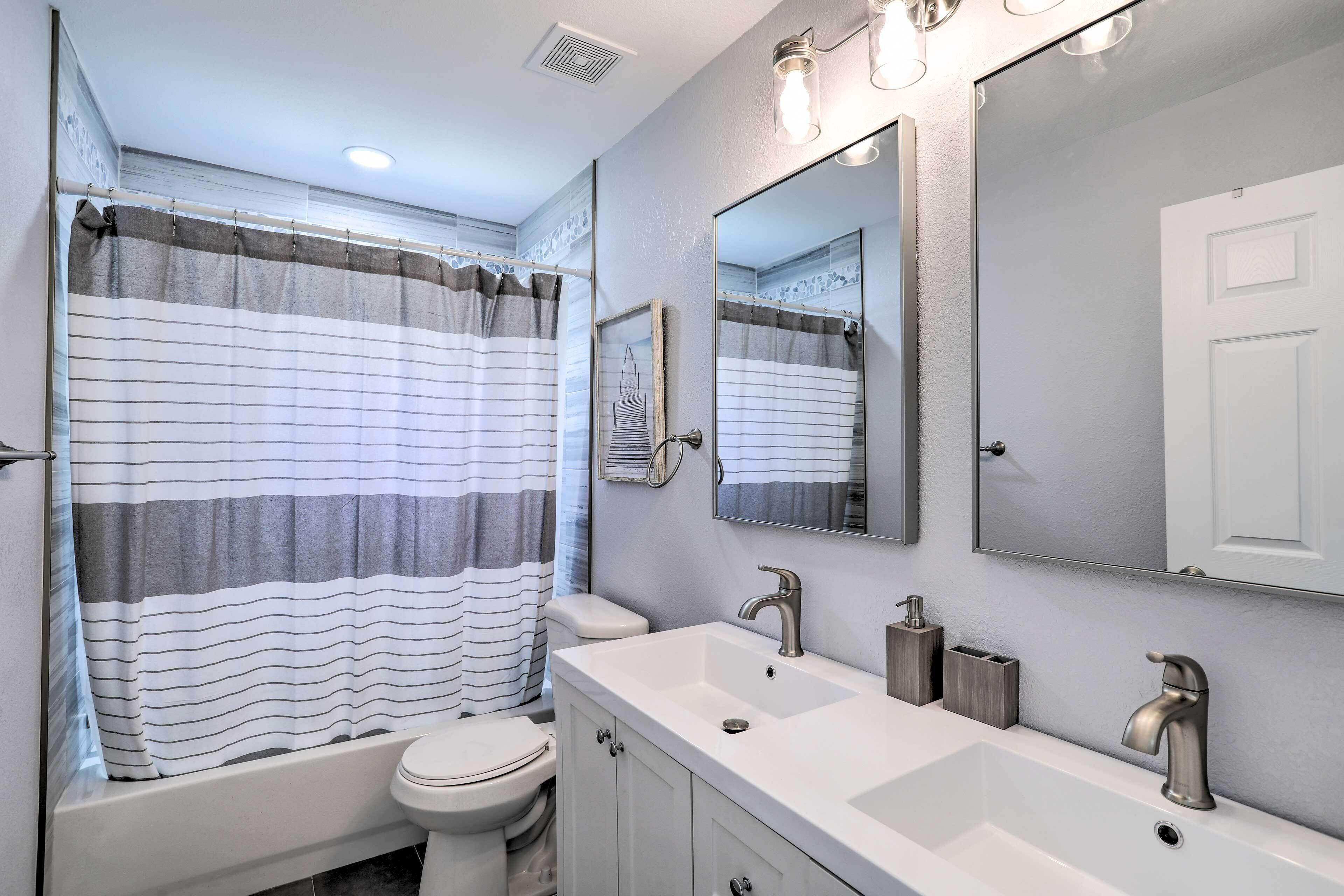 Un baño moderno con un lavabo blanco, dos grifos, un espejo y una cortina de ducha a rayas.