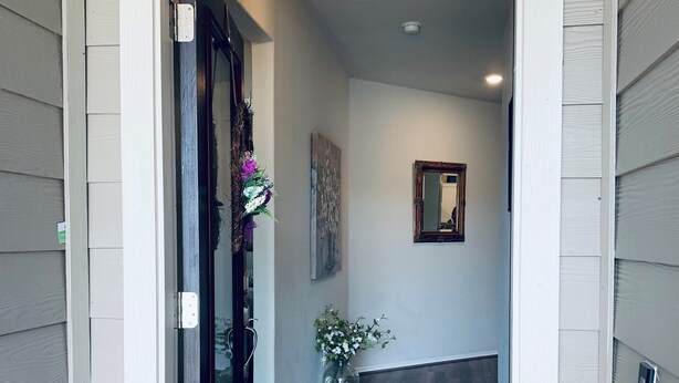 Un pasillo con piso de madera, una puerta con panel de vidrio, una lámpara colgante y un florero con flores.