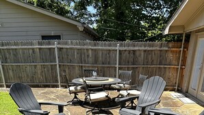 Ein Hinterhof mit einer Terrasse, Adirondack-Stühlen, einem runden Tisch und einem Kamin aus Stein.