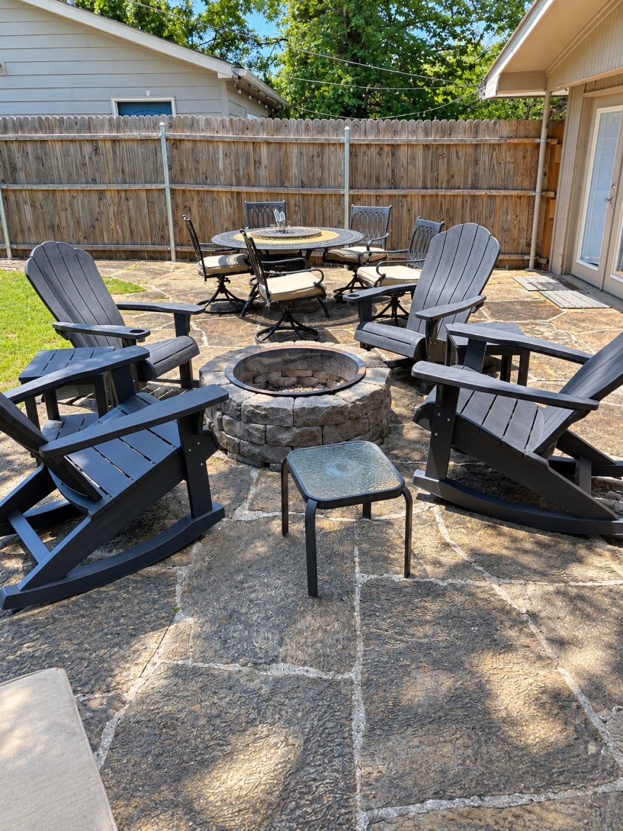 An outdoor patio with Adirondack chairs, a stone fire pit, and a stone table.