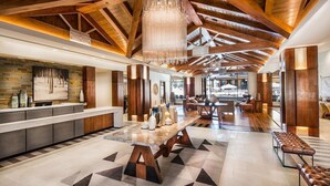 A spacious lobby with a high ceiling, wooden beams, a central seating area, and a modern chandelier.