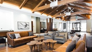 A spacious lobby with wooden flooring, leather sofas, and round coffee tables.