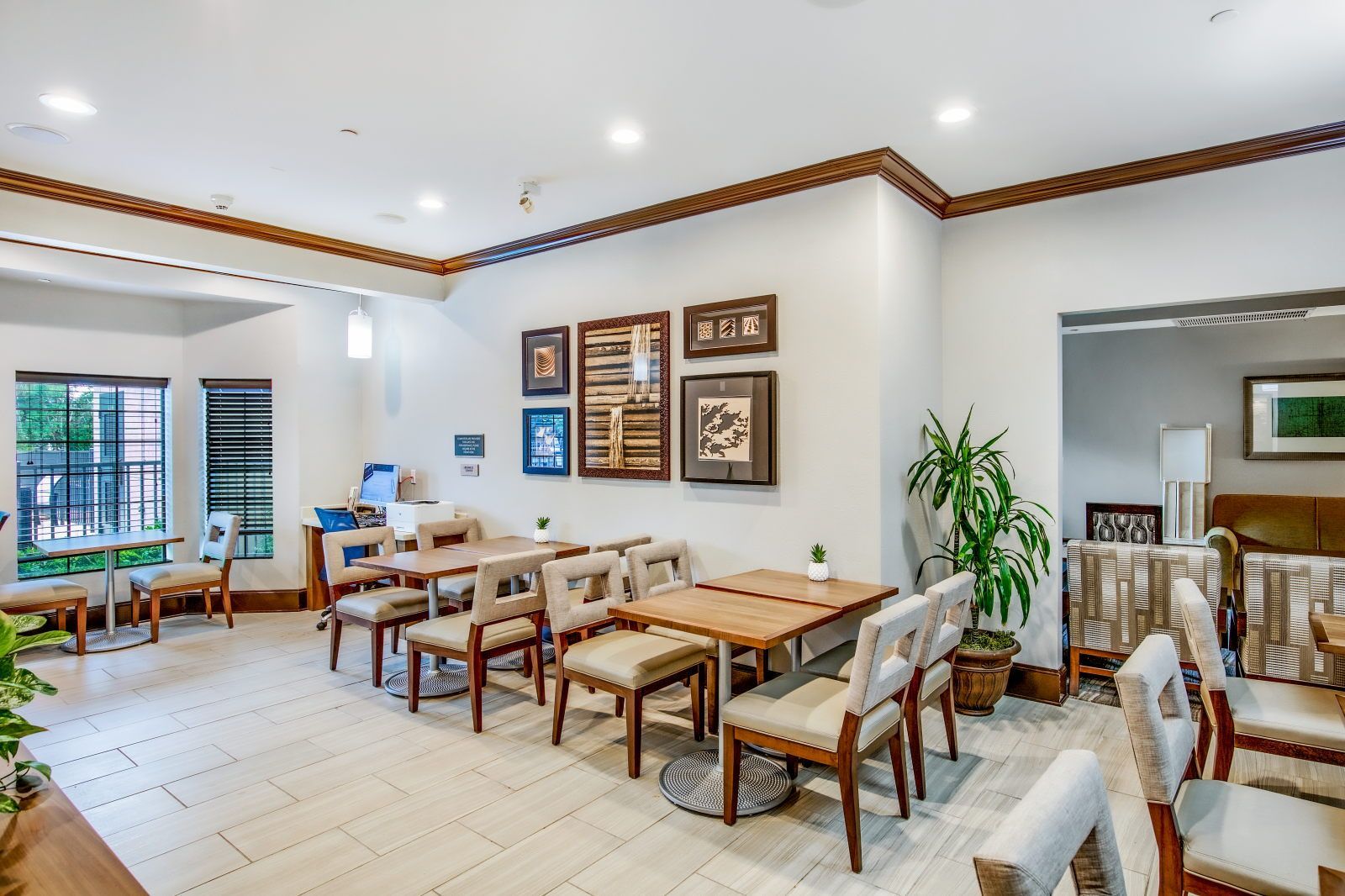 A spacious dining area with multiple tables and chairs, framed artwork on the walls, and a large window providing natural light.