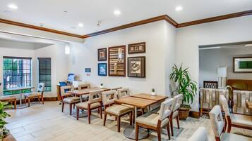 A spacious dining area with multiple tables and chairs, framed artwork on the walls, and a large window providing natural light.