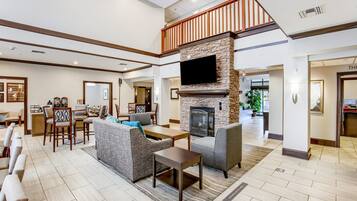 A spacious hotel lobby with a fireplace, seating area, and a television mounted on the wall.