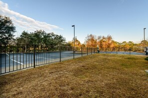 Een basketbalveld buiten, omringd door bomen en gras, met een metalen hek.