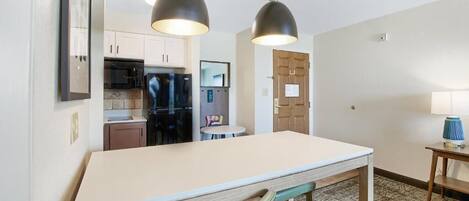 A compact kitchen with a central island, overhead pendant lights, and a small dining table.