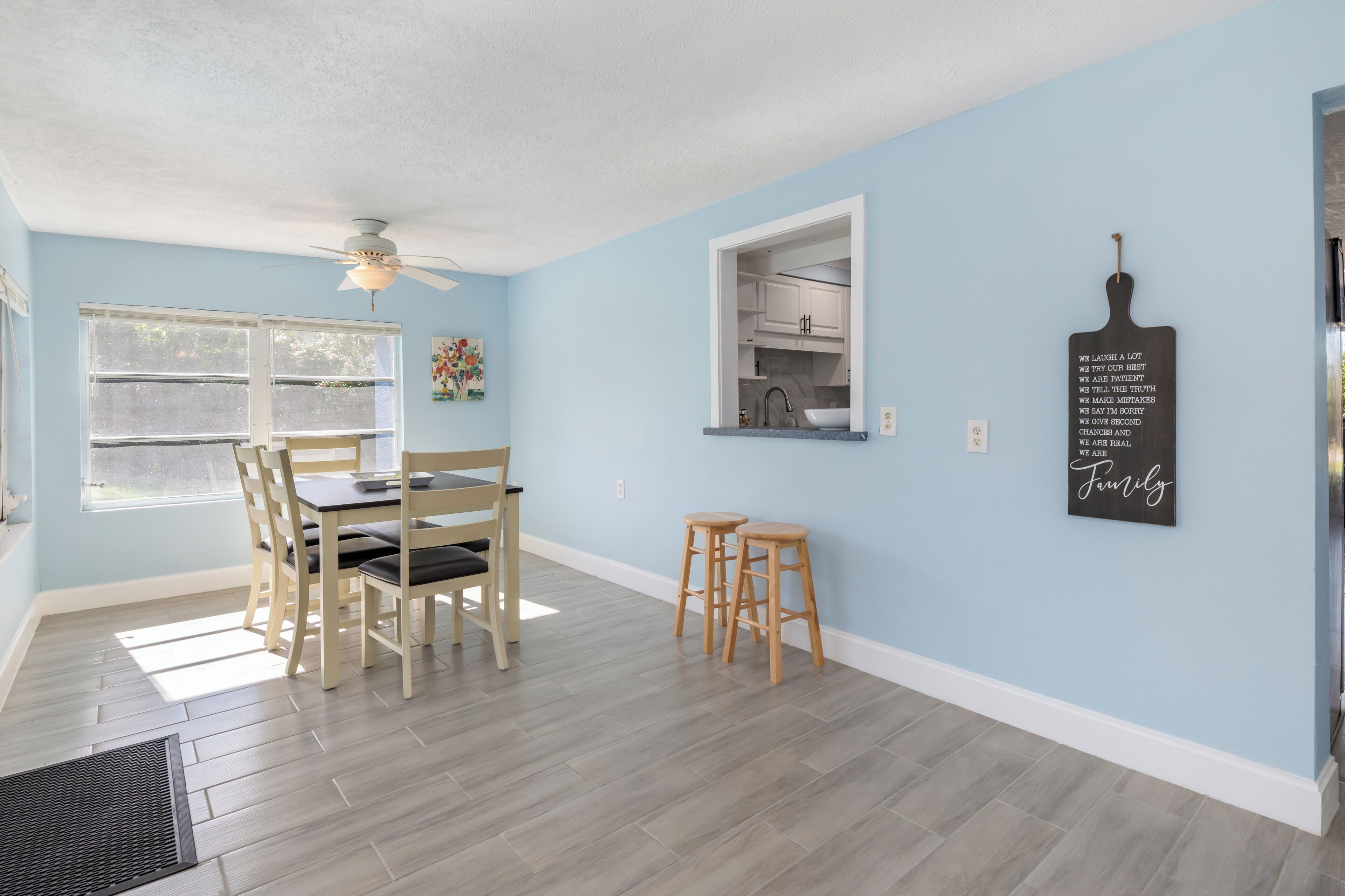 A dining area with a table and chairs, a ceiling fan, a window, and a kitchen visible through an open door.
