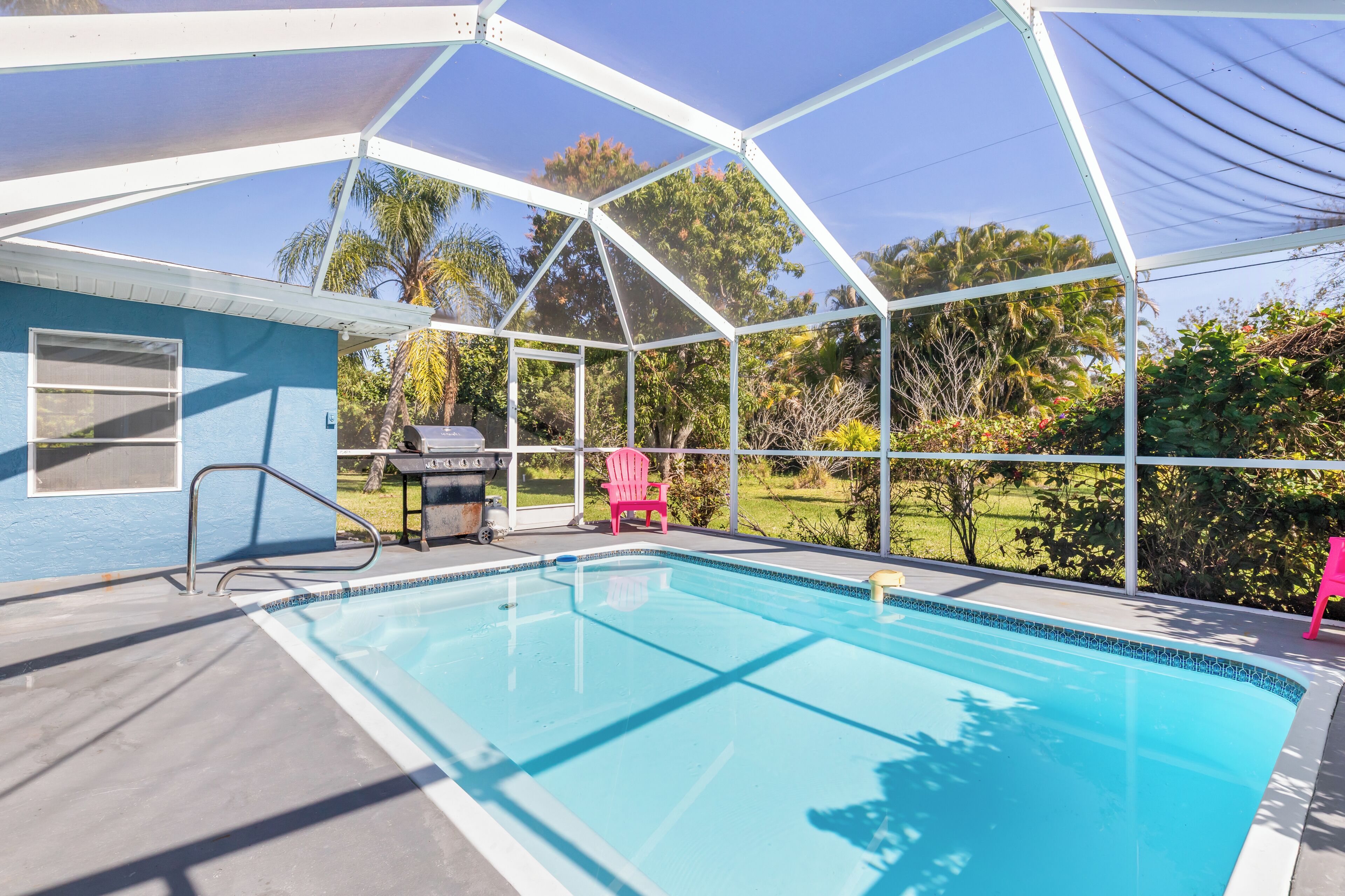 A covered swimming pool with a patio area, a grill, and a pink chair.