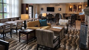 A spacious lobby with a mix of seating areas, including sofas and chairs, a dining area with tables, and a flat-screen TV mounted on the wall. - Free Breakfast Buffet. Pool, Hot Tub & Gym Access! (Novi)